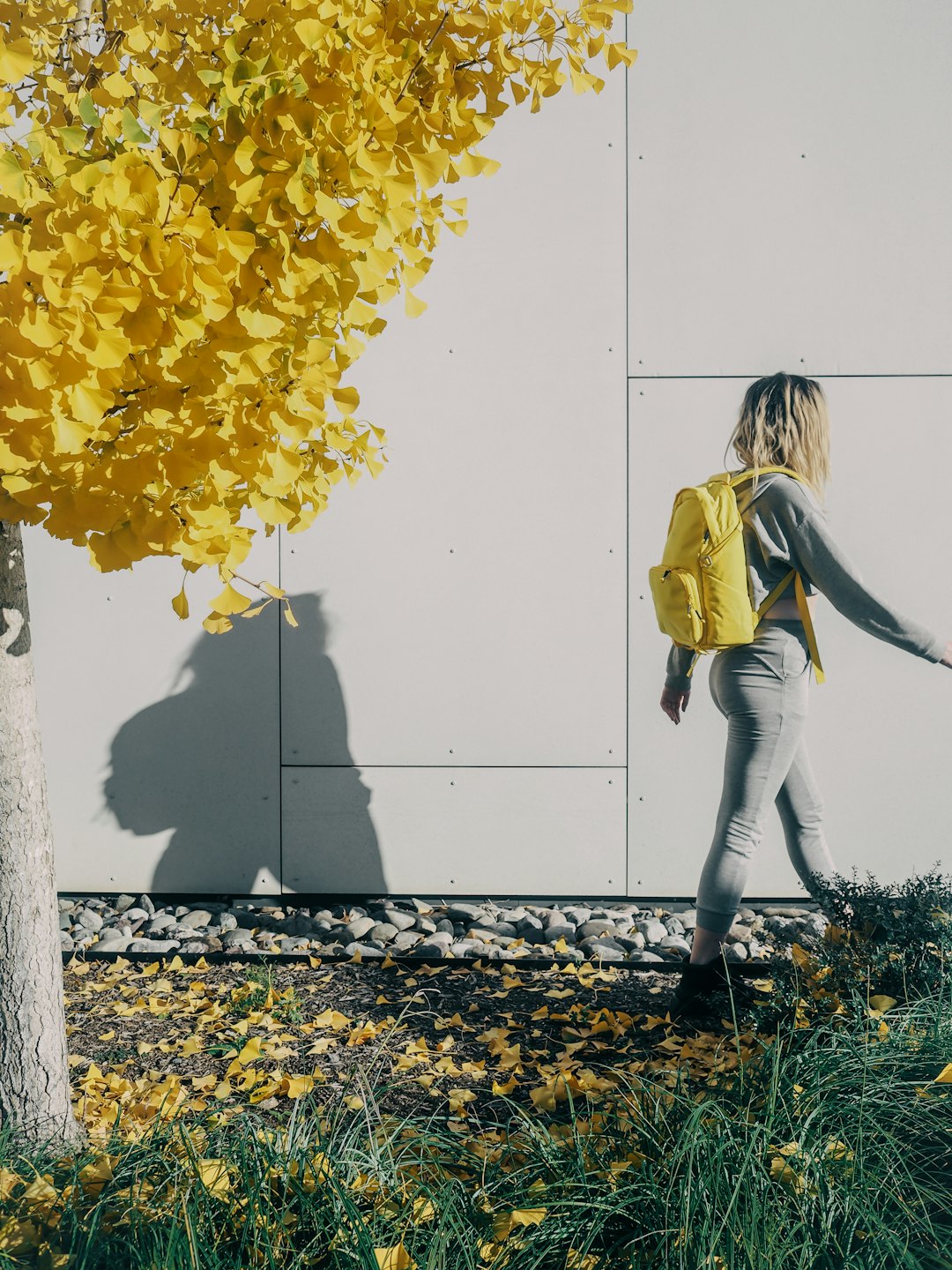 woman in yellow jacket and gray pants standing beside white wall