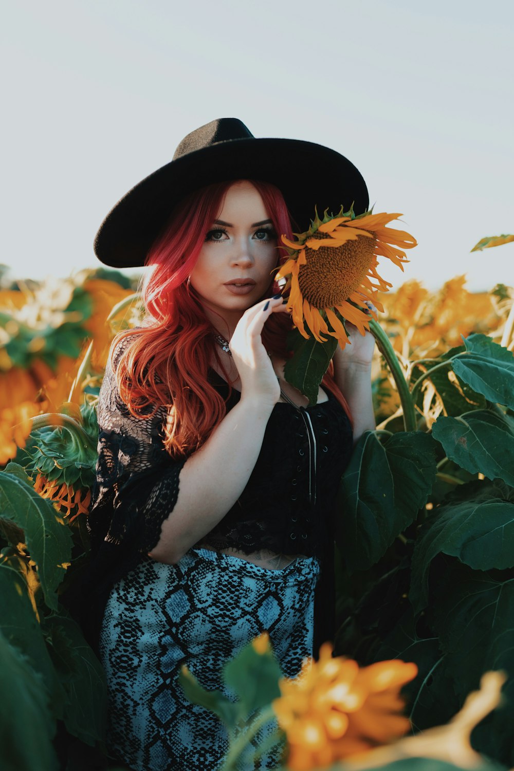 woman in black and white floral dress wearing black sun hat standing on sunflower field during