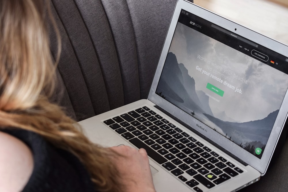 person using macbook air on gray couch