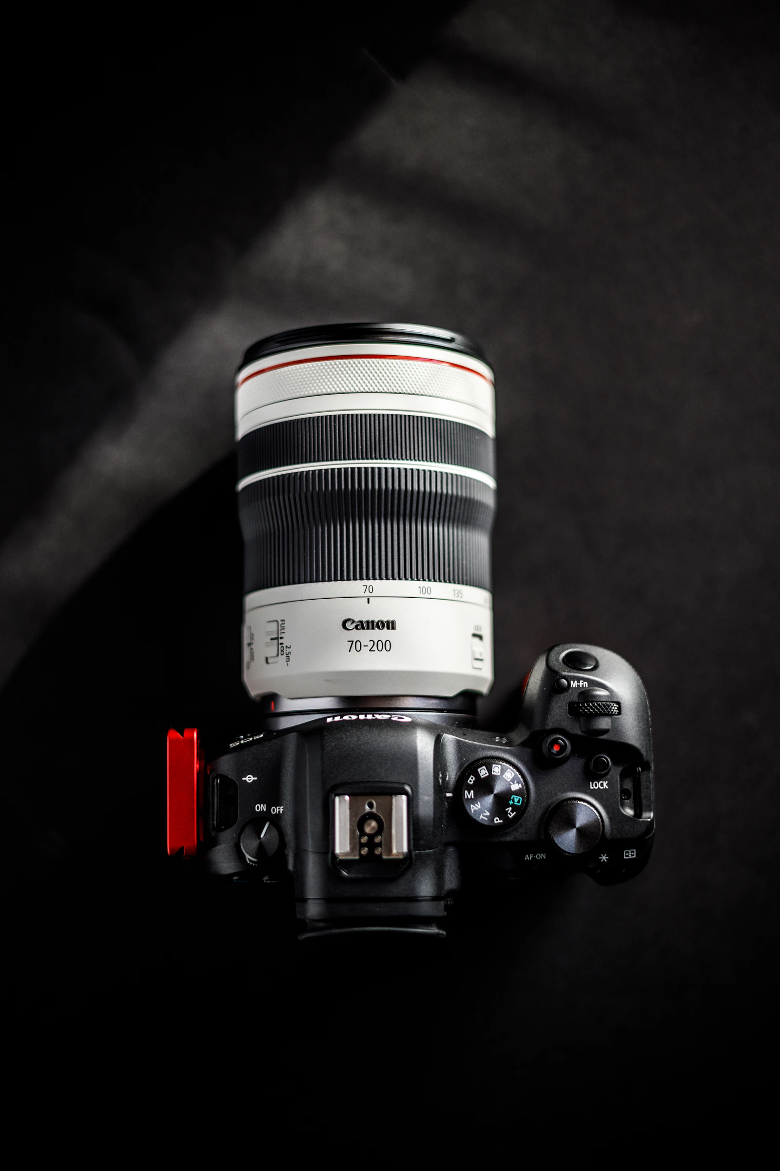 A mirrorless camera with a white 70-200 mm zoom lens, photographed from directly above on a dark background, showing the power lever, hot shoe, mode dial and shutter button