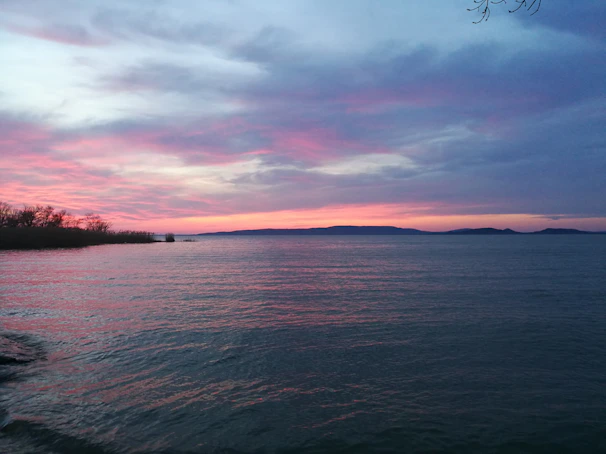 A serene lakeside at sunset with soft pink and orange hues reflecting on the water.