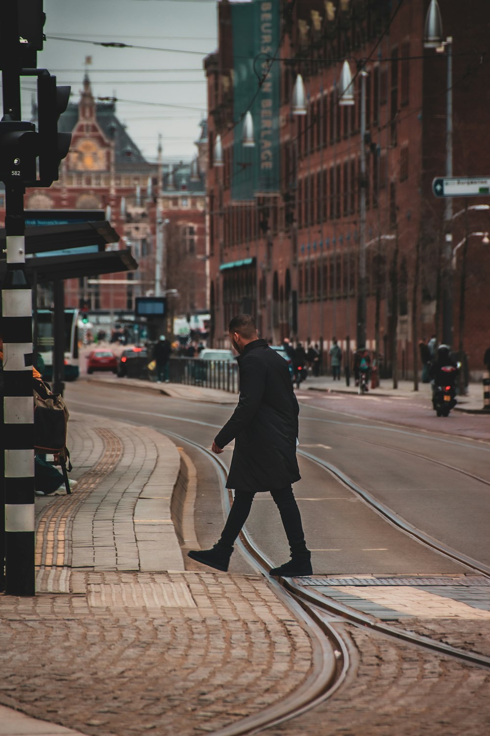 homme en manteau noir marchant sur une voie piétonne pendant la journée