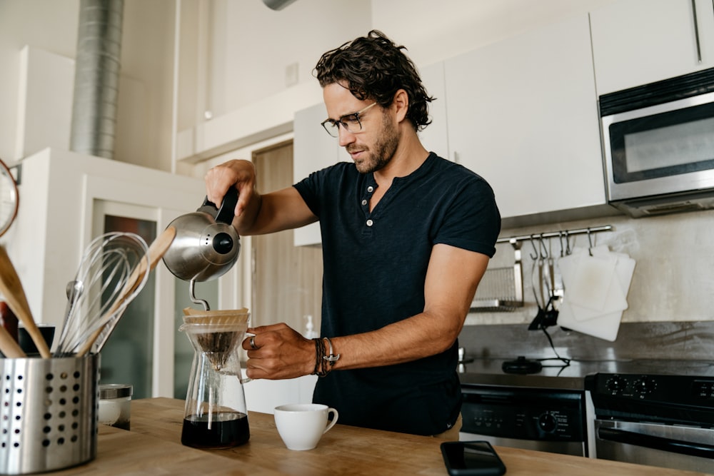 homme en t-shirt à col rond bleu versant de l’eau sur une tasse à thé en céramique blanche