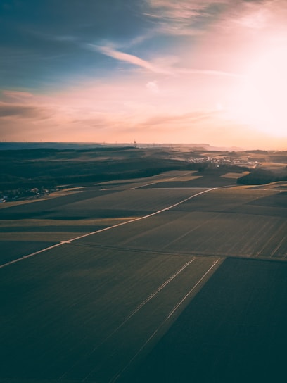 Aerial view of a drone flying over lush agricultural fields at sunrise.