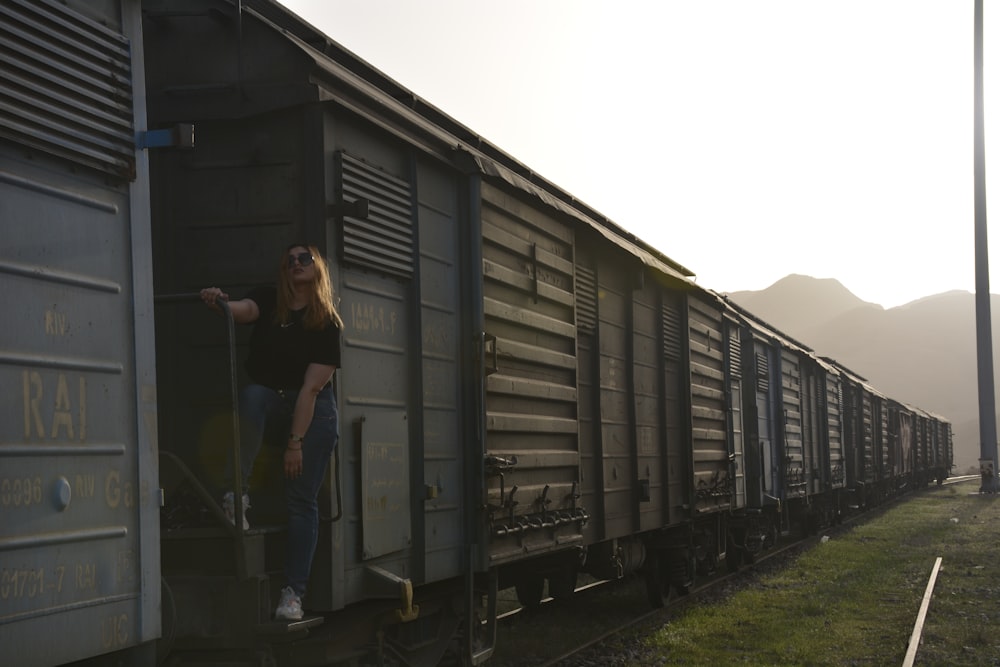 woman in black jacket standing beside gray steel cargo trailer during daytime
