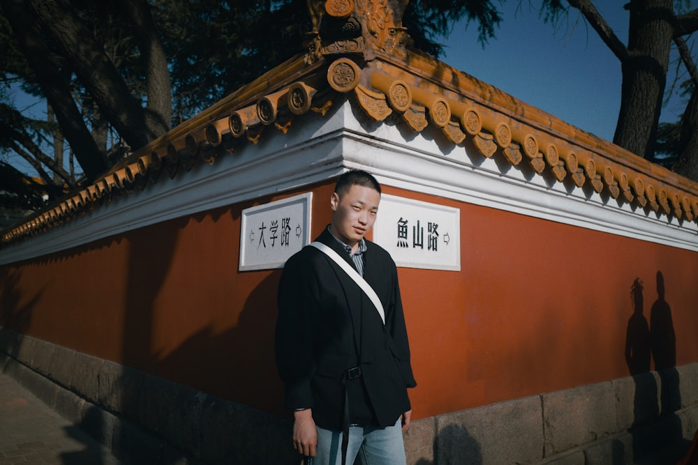 man in black blazer standing near orange building during daytime