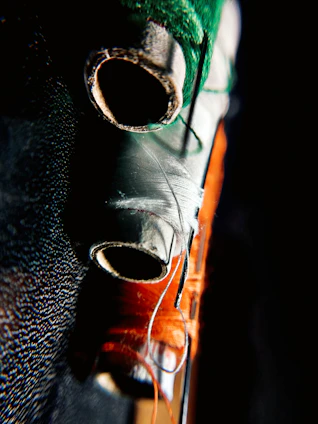 Close-up of a colorful embroidered fabric bag resting beside sewing threads and needles on a wooden table.