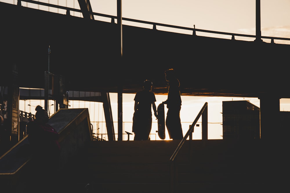 silhouette of 2 person standing on wooden dock during daytime