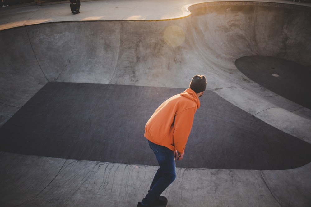 man in orange hoodie and black pants walking on gray concrete floor