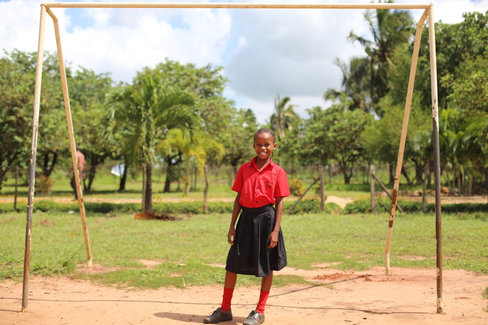 boy in red polo shirt and black skirt standing on brown soil during daytime