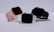Three smartwatches are displayed on a light background. They feature different colored bands: pink, white, and black. The watches have large, rectangular touchscreens, and they are positioned to show off their sleek and modern design.