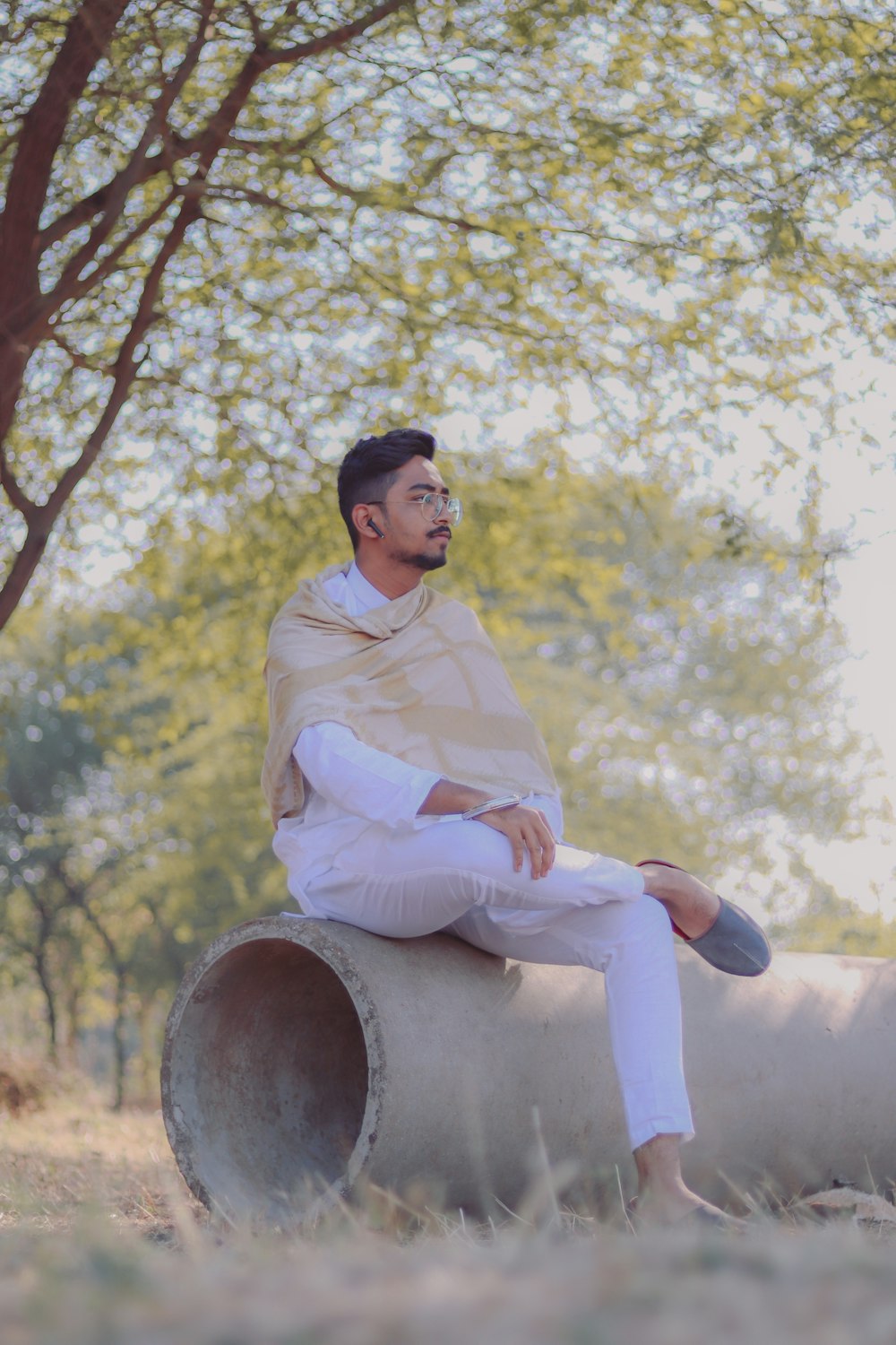 man in white dress shirt sitting on brown wooden barrel under yellow leaf tree during daytime