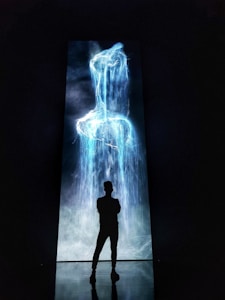 A silhouette of a person stands in front of a tall, vertical digital display showcasing vibrant blue and white light resembling a waterfall or abstract liquid flow against a dark background.