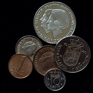 A collection of various coins featuring inscriptions and profiles of a woman, likely a royal figure. The coins display different sizes and engravings, including dates such as 1980 and 1960, and words like 'Nederland' and 'Koningin.'