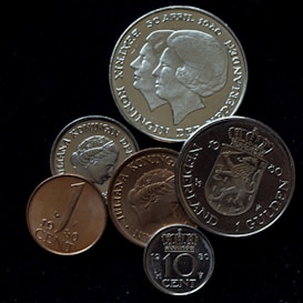 A collection of various coins featuring inscriptions and profiles of a woman, likely a royal figure. The coins display different sizes and engravings, including dates such as 1980 and 1960, and words like 'Nederland' and 'Koningin.'