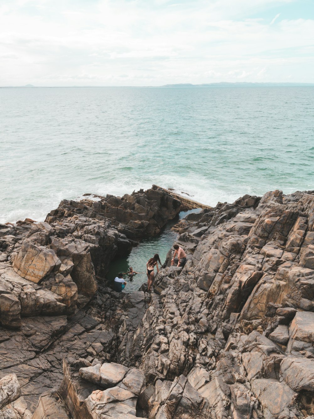 personnes assises sur une formation rocheuse près de la mer pendant la journée