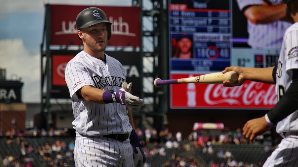 man in white and black baseball jersey shirt holding baseball bat