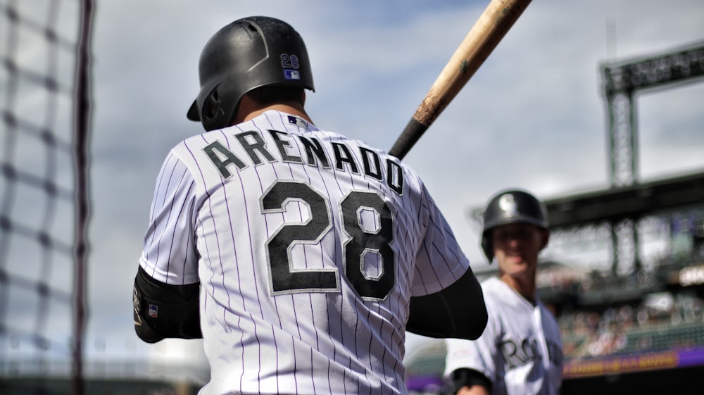 man in white and black baseball jersey shirt holding baseball bat