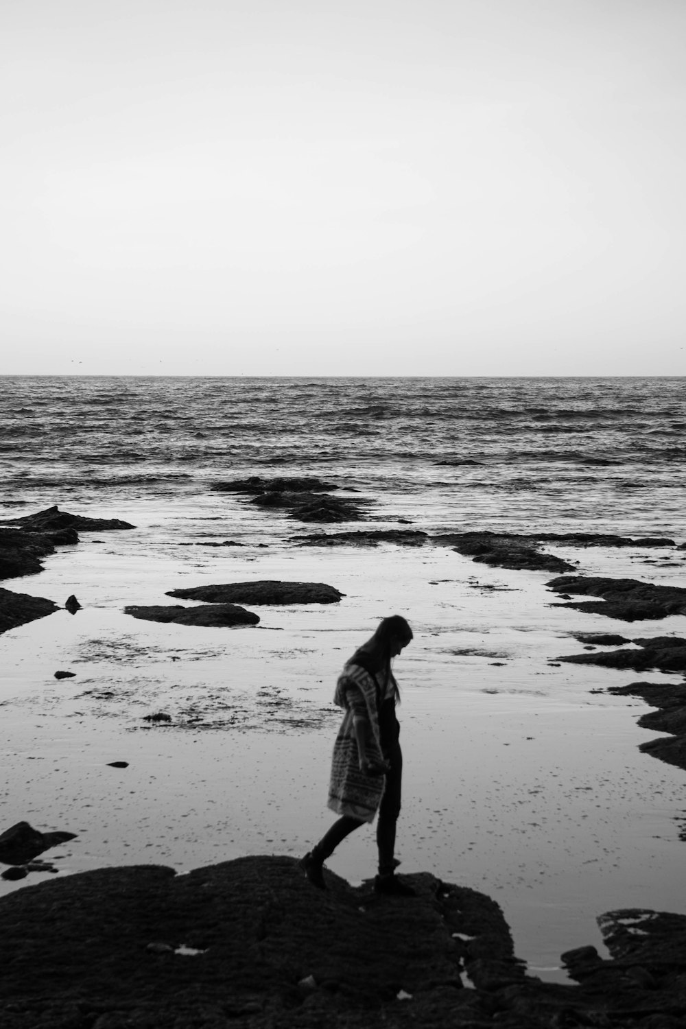 grayscale photo of girl standing on seashore