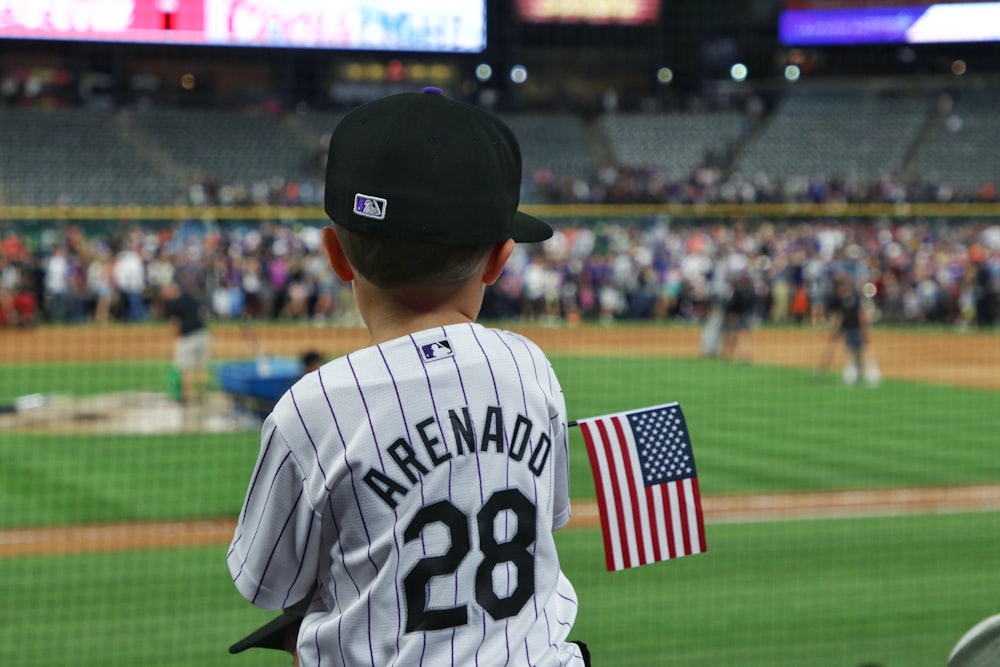 man in white and black baseball jersey shirt holding us a flag