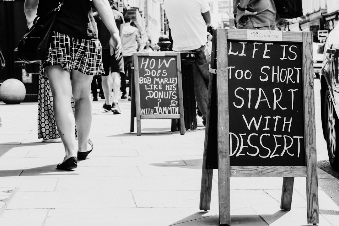 grayscale photo of woman in mini skirt standing near wooden signage
