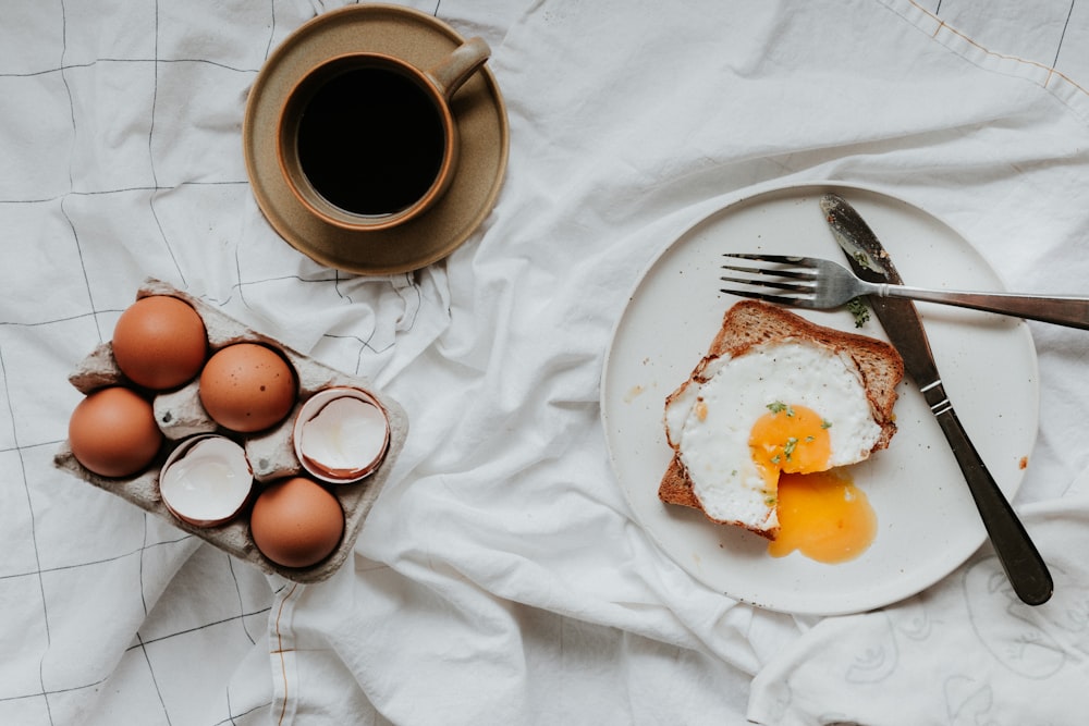 oeuf sur assiette en céramique blanche à côté d’une fourchette et d’un couteau en acier inoxydable