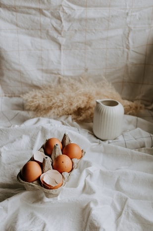 Close-up of a glass of creamy milk beside a rustic wooden crate filled with farm eggs