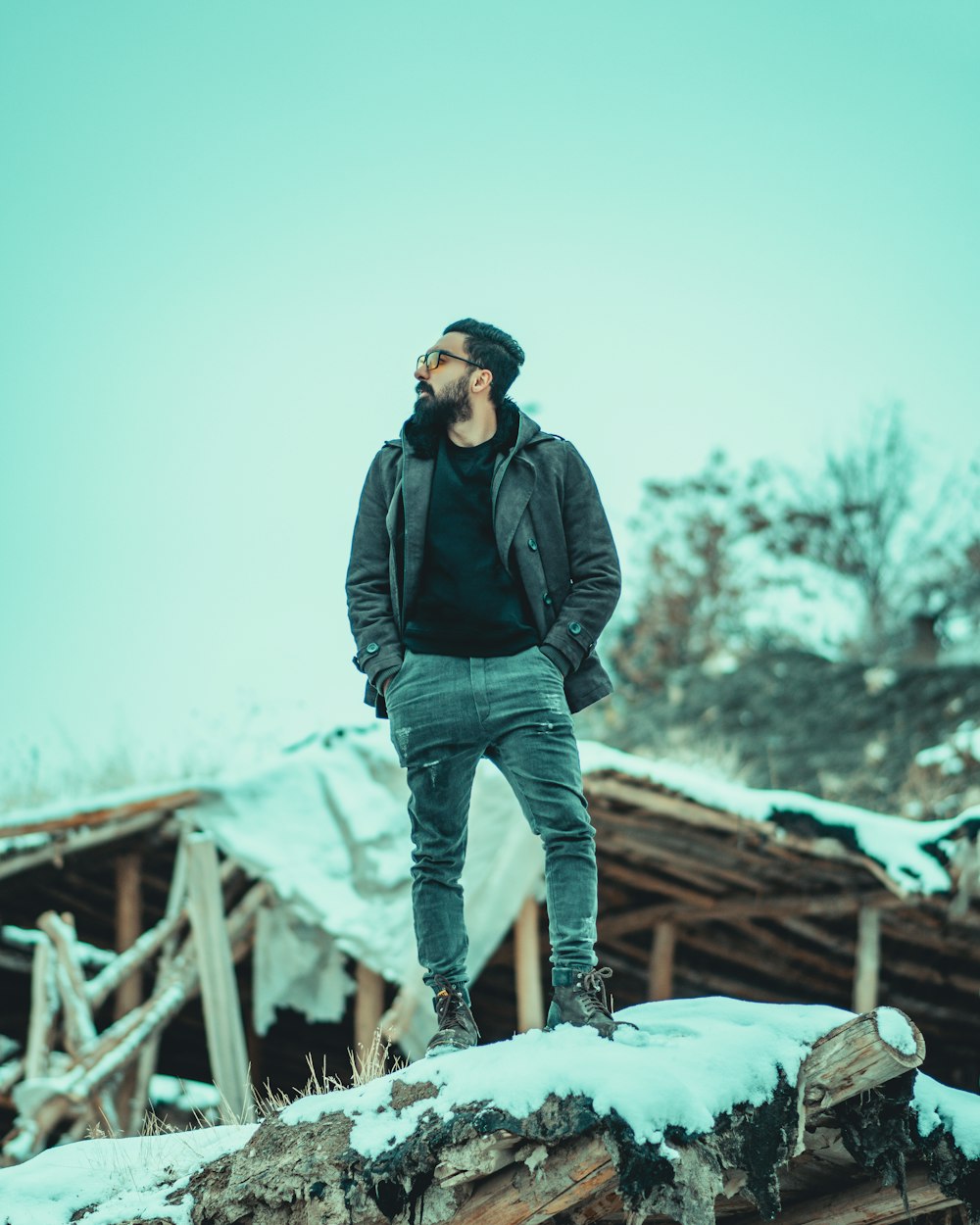 man in black jacket and blue denim jeans standing on snow covered ground during daytime