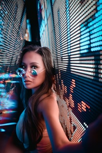 A person wearing reflective sunglasses is positioned between two walls displaying bright, colorful LED lights. The lights create an immersive, futuristic environment with a focus on neon hues.