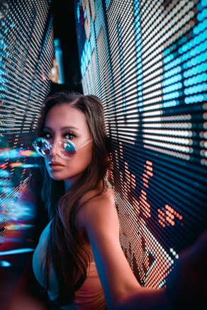 A person wearing reflective sunglasses is positioned between two walls displaying bright, colorful LED lights. The lights create an immersive, futuristic environment with a focus on neon hues.