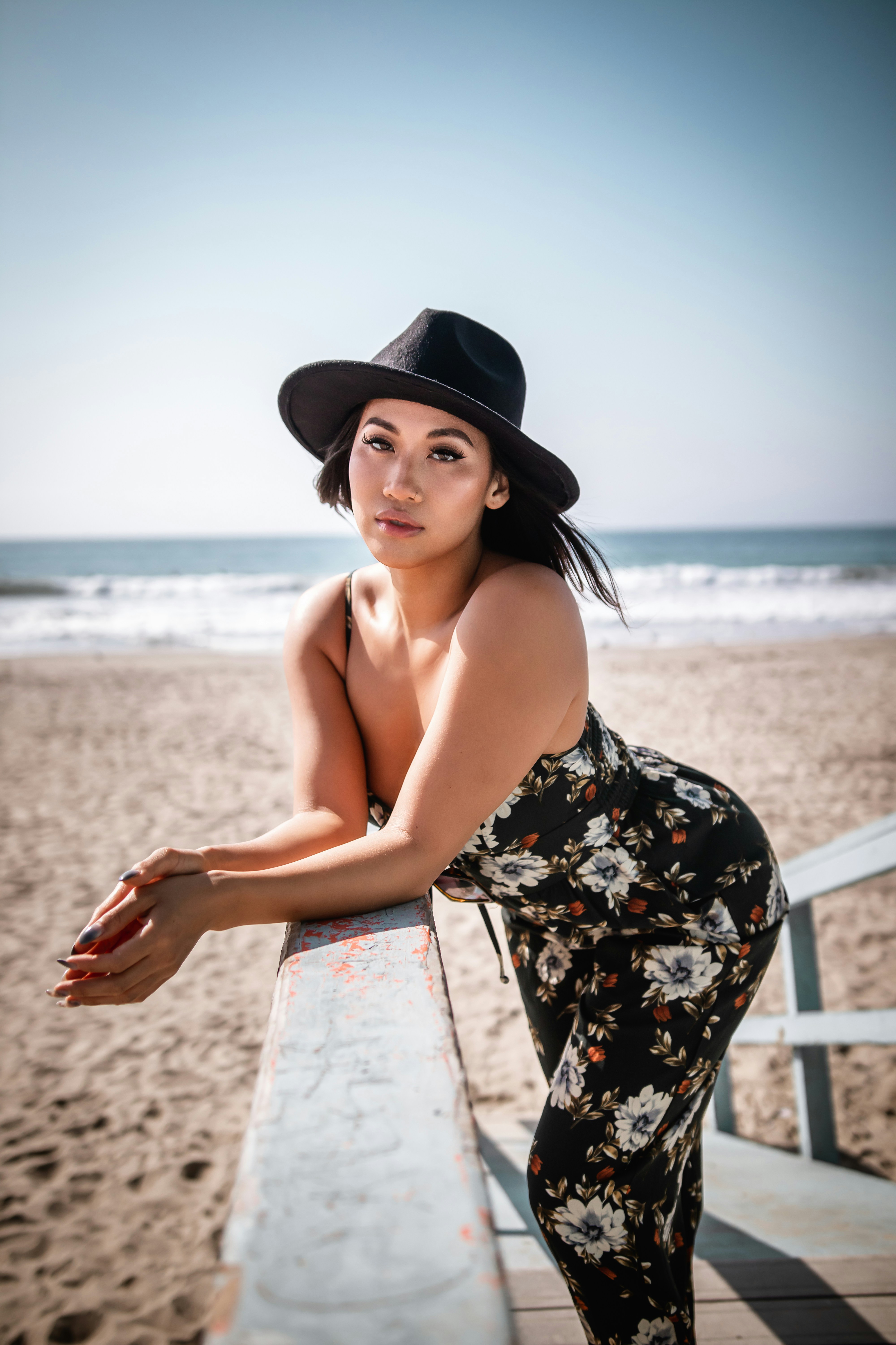 Frau in schwarz-weißem Blumenschlauchkleid mit schwarzem Hut, die tagsüber am Strand steht