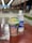A cup of instant noodles labeled 'Pop Mie' sits on a table next to a bottle of Pocari Sweat. Several small packets, possibly seasoning or utensils, are also present on the table. The background appears to be a blurred indoor setting with tables and lights.