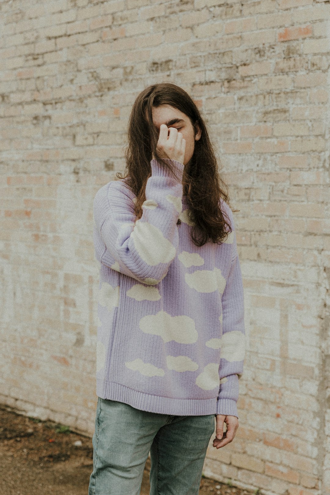 woman in white and purple polka dot long sleeve shirt covering her face with her hands