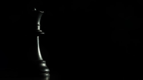A chess queen is placed prominently on the left side, emerging from the shadows with a metallic sheen against a dark, minimalist background.