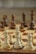 A close-up view of a chessboard with wooden chess pieces arranged in starting positions, featuring pawns, knights, bishops, rooks, a queen, and a king in focus. The foreground pieces are made of light wood while the background pieces are darker, out of focus.