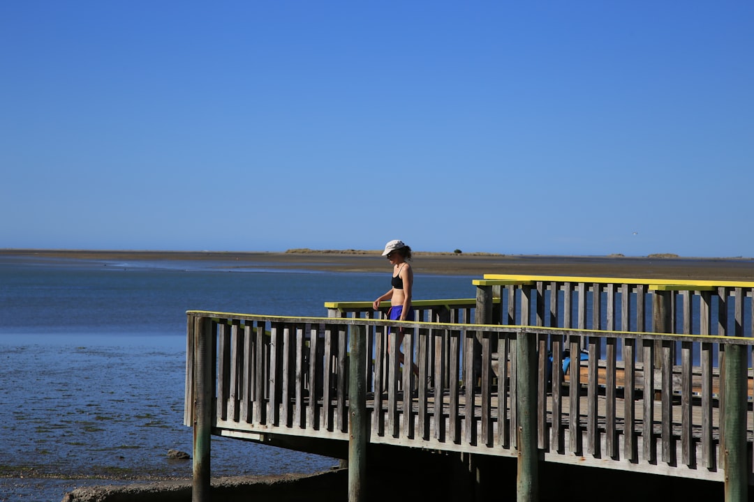 woman in black tank top sitting on brown wooden railings by the sea during daytime