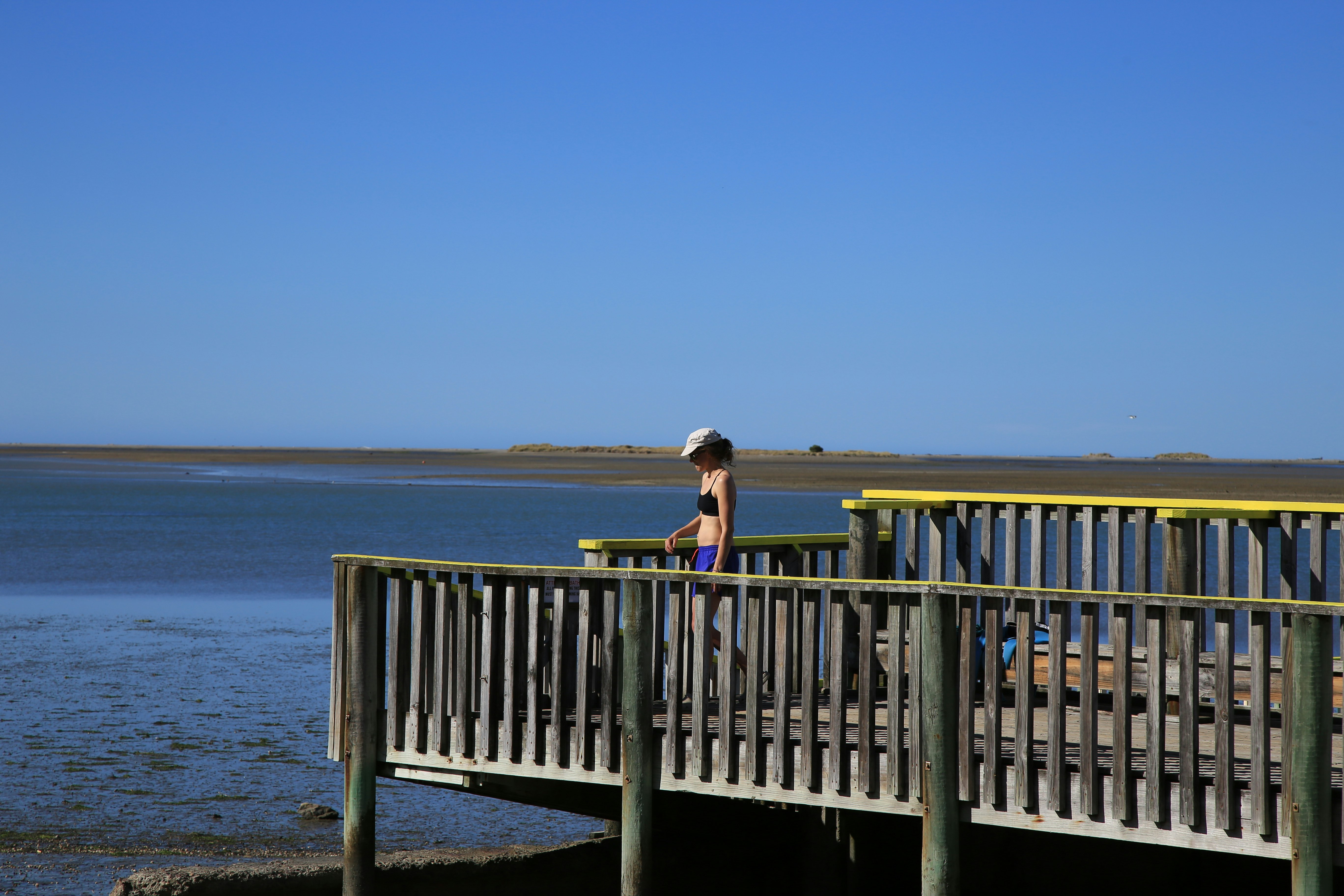 woman in black tank top sitting on brown wooden railings by the sea during daytime