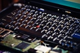 A close-up view of a laptop keyboard with one of the keycaps missing, revealing internal components beneath. The focus is on the details of the keys and the circuitry visible underneath.