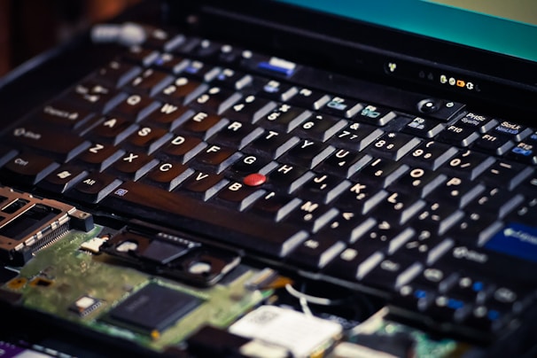 A close-up view of a laptop keyboard with one of the keycaps missing, revealing internal components beneath. The focus is on the details of the keys and the circuitry visible underneath.