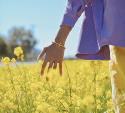 person in brown long sleeve shirt standing on yellow flower field during daytime