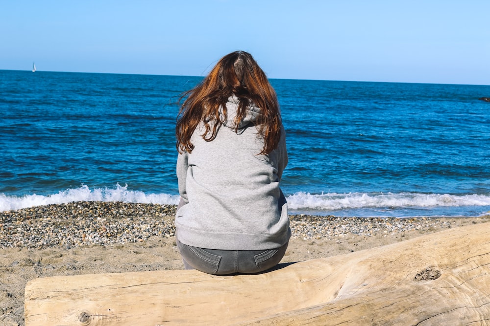 woman in white long sleeve shirt sitting on brown concrete wall near body of water during