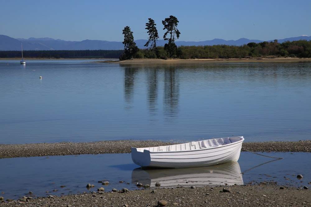 barco branco na areia marrom perto do corpo de água durante o dia