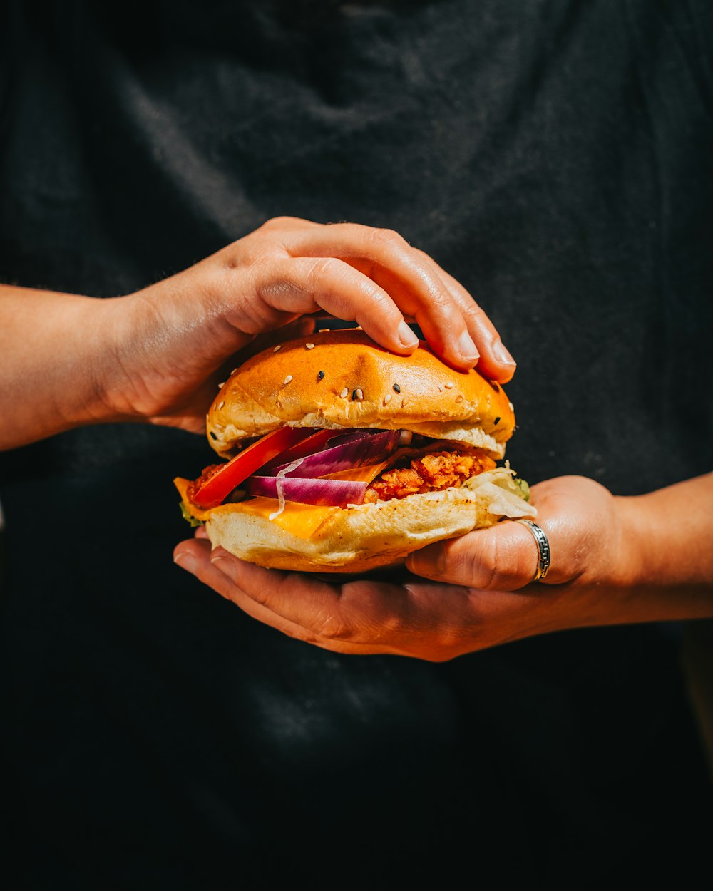 person holding burger with tomato and lettuce