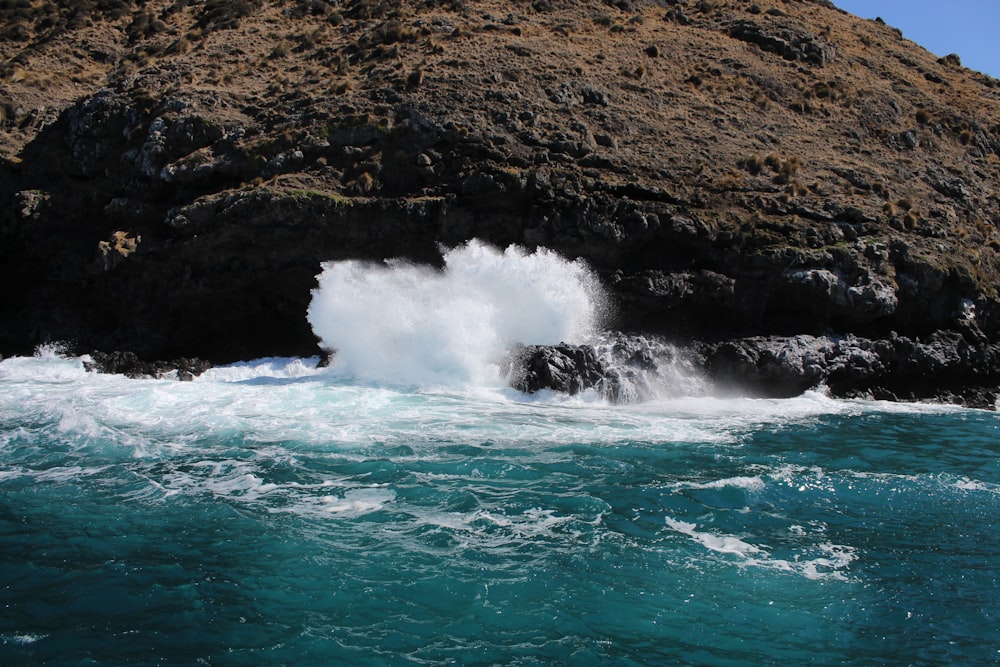 ondas do oceano batendo em formação rochosa marrom durante o dia