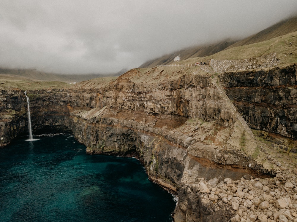 brown rocky mountain beside blue sea under white clouds during daytime