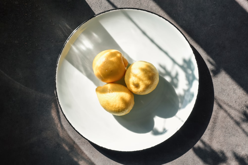 three yellow round fruits on white ceramic plate
