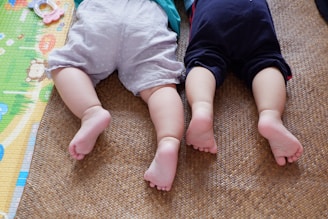 baby in white shirt and black pants lying on brown carpet