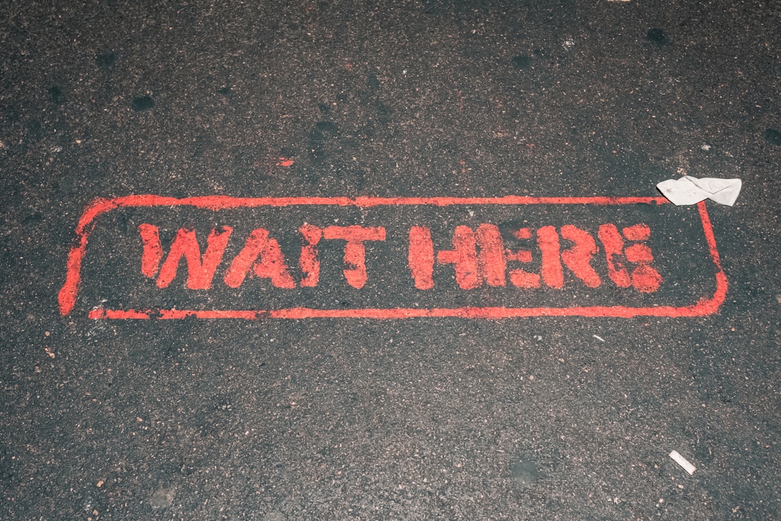 a red street sign that reads wait here