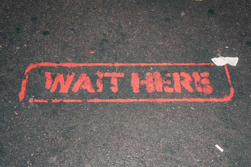 a red street sign that reads wait here