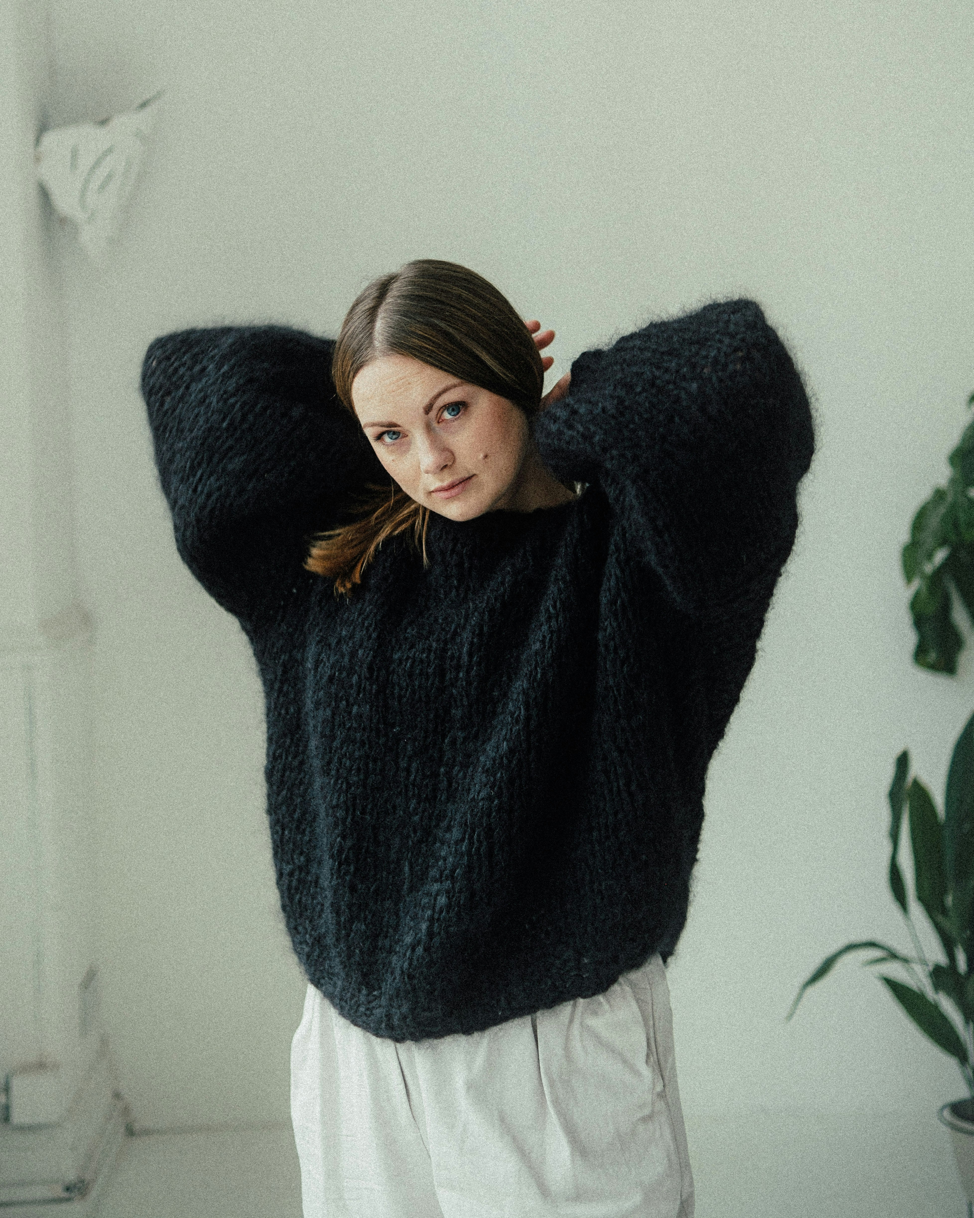 Woman wearing a chunky dark sweater posing against a wall.